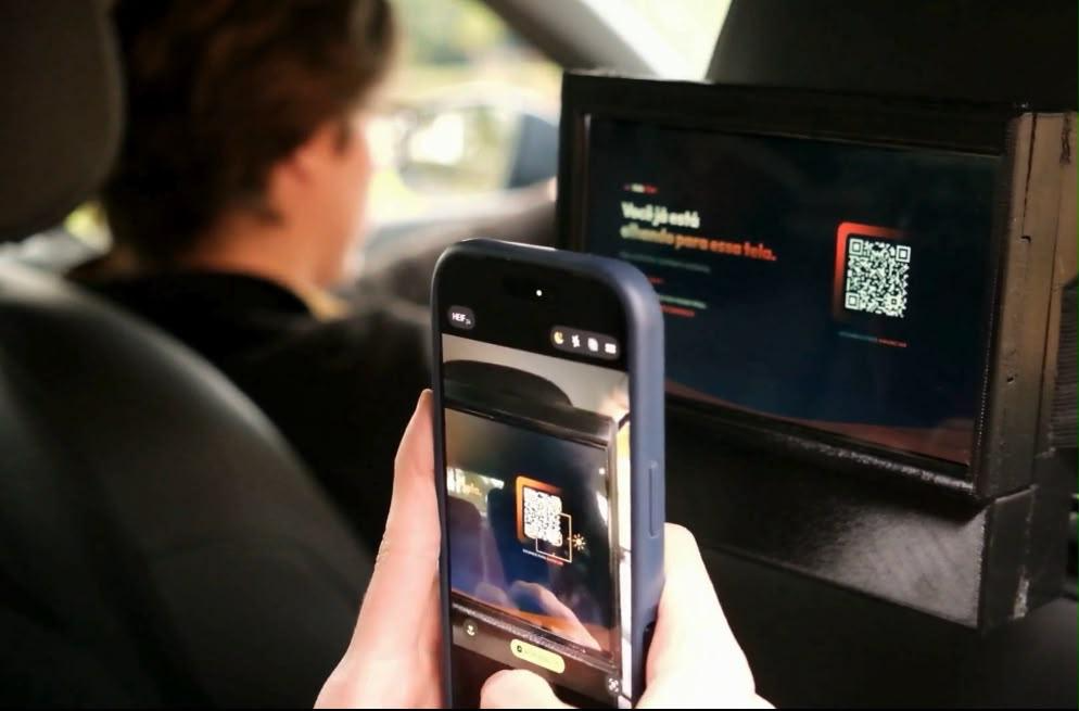 Passageiro escaneando QR Code da tela AdsCar com o celular dentro do veículo